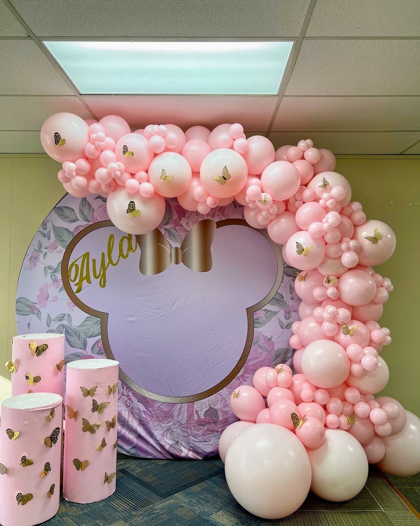 A bunch of pink balloons are sitting in front of a mickey mouse backdrop.