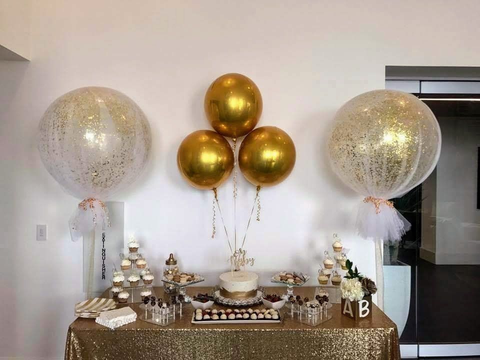 A table decorated with gold and white balloons and cupcakes.