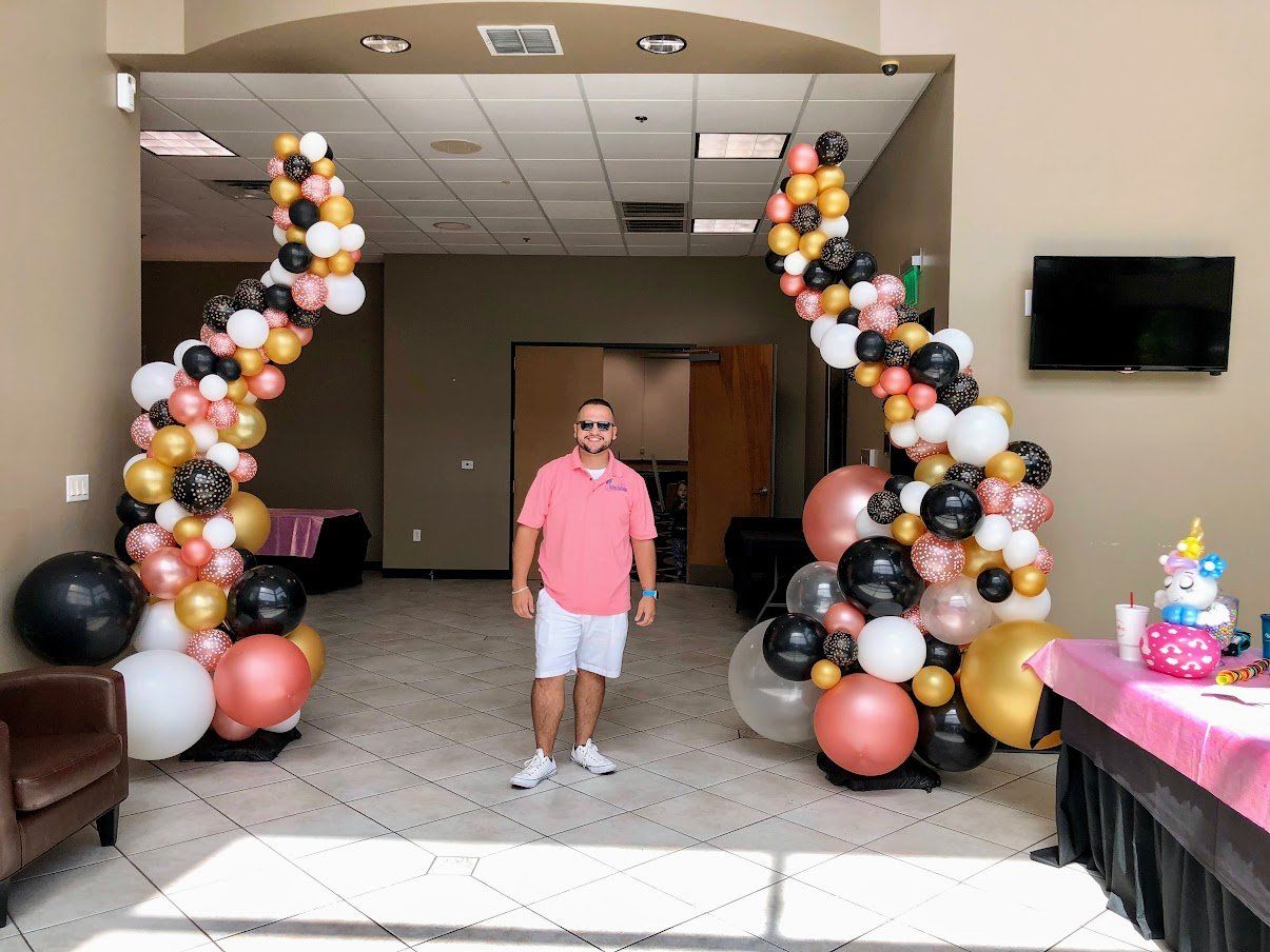 A man is standing in front of a balloon arch in a room.