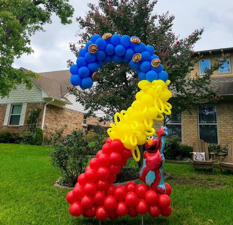 Elmo is standing next to a number 2 made of balloons in front of a house.