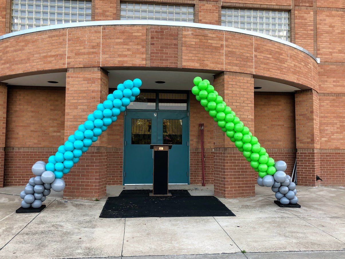A blue and green balloon arch is in front of a brick building.