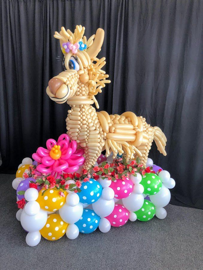 A llama made out of balloons is surrounded by balloons and flowers