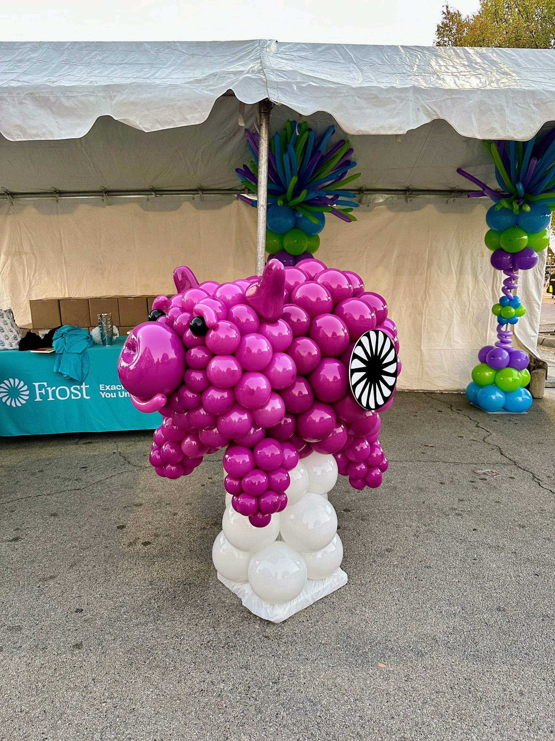 purple balloon piggy bank balloon sculpture with the Frost bank logo in front of a tent used for an outer market
