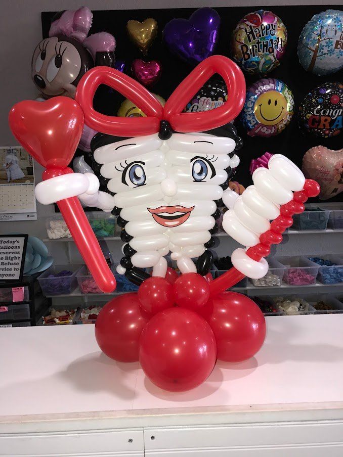 A tooth made out of balloons is holding a toothbrush and a heart