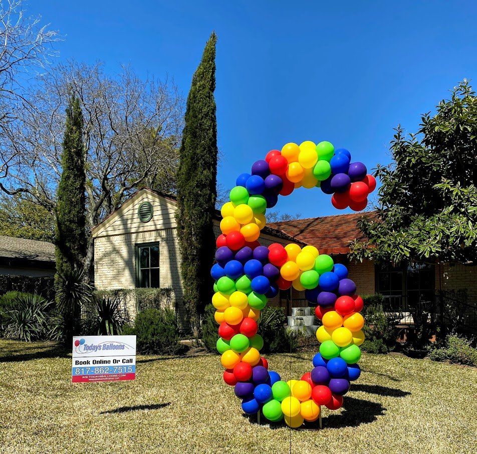 A large letter g made of colorful balloons in front of a house.