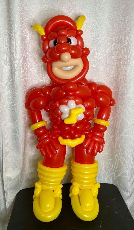 A superhero made out of red and yellow balloons is sitting on a table.
