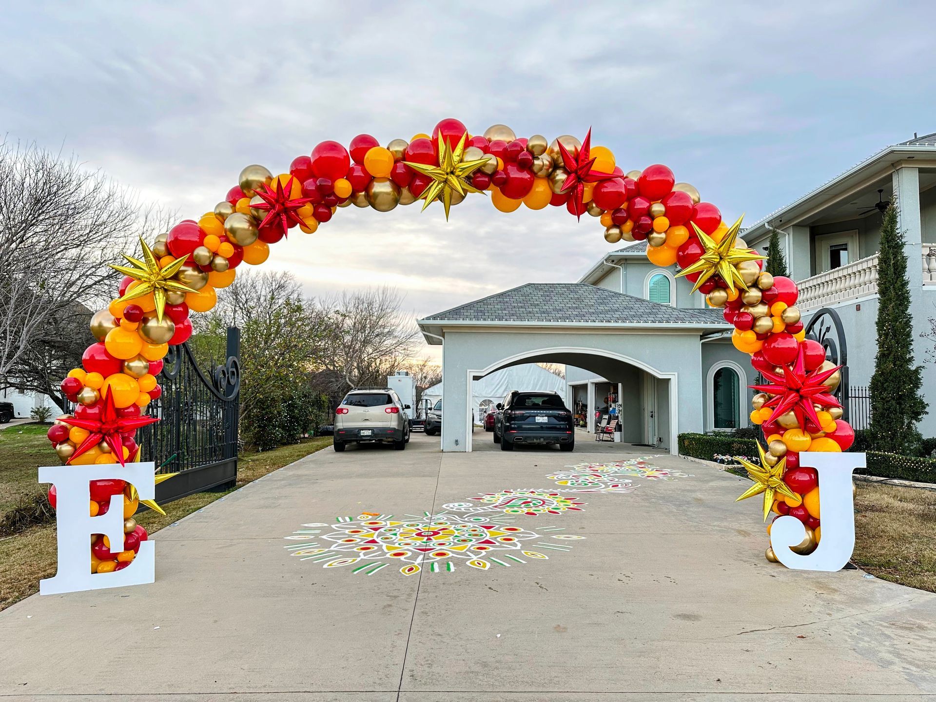 balloon arch in red, yellow and gold balloons with starburst balloon accents in driveway.