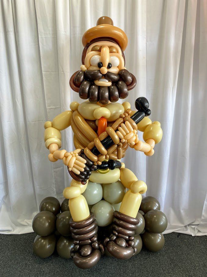 A statue of a man made out of balloons is sitting on a pile of balloons.