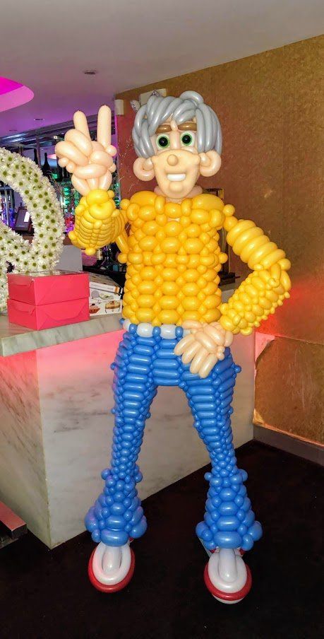 A statue of a man made out of balloons is standing in a room.