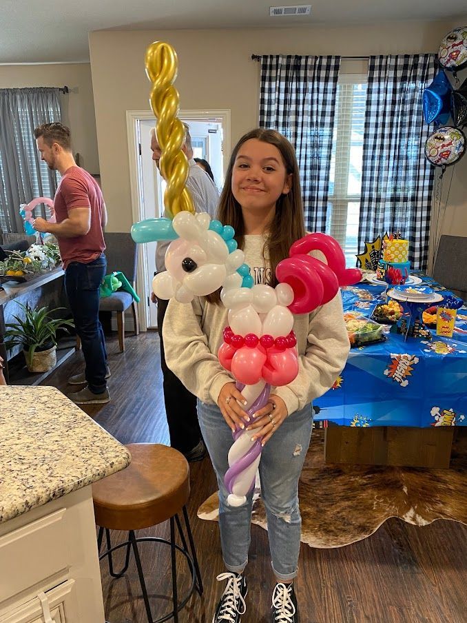 A girl is holding a balloon in the shape of a unicorn.