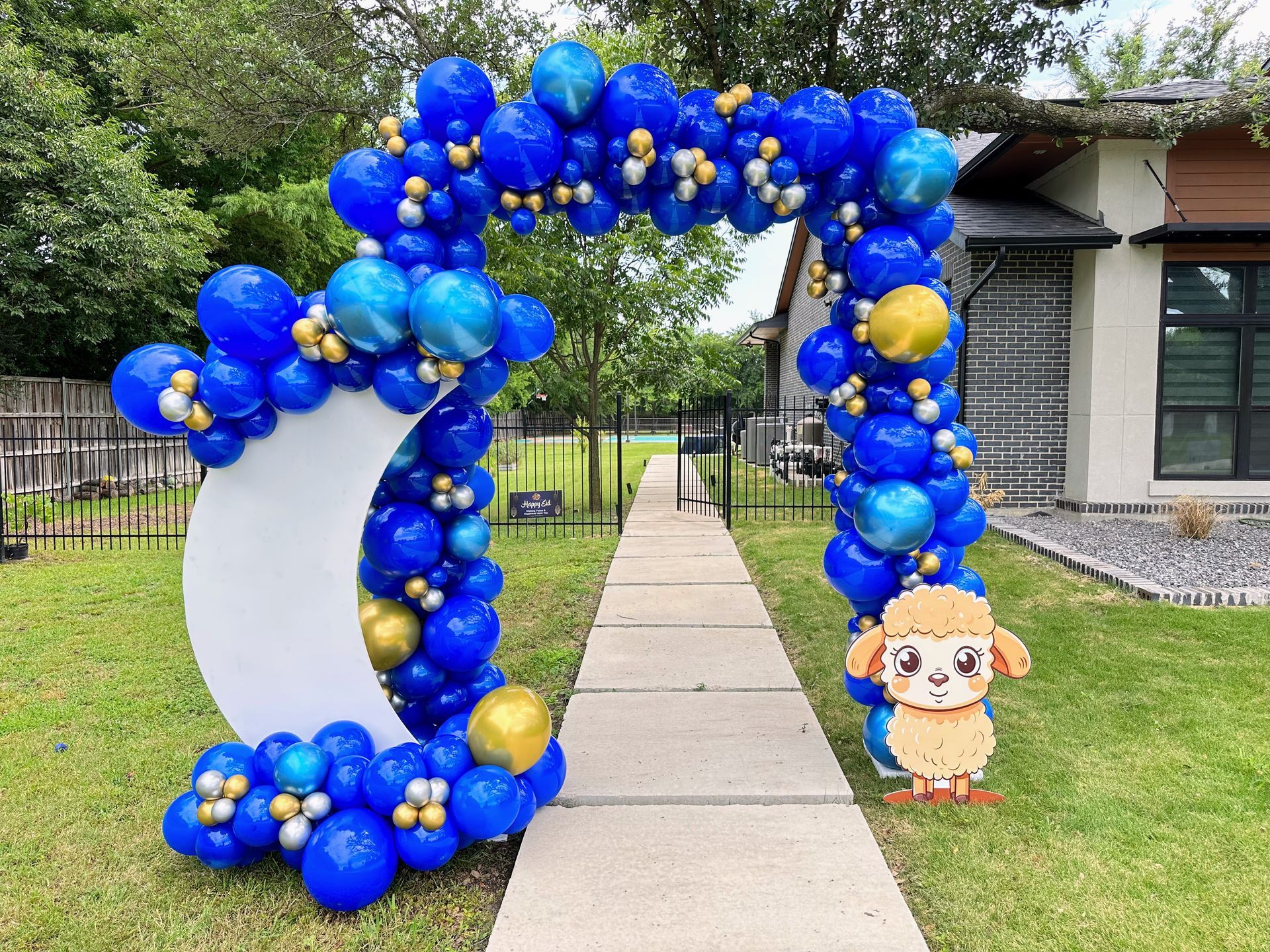 A blue and gold balloon arch is sitting on the sidewalk in front of a house.
