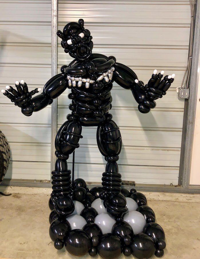 A robot made out of balloons is standing in front of a garage door.