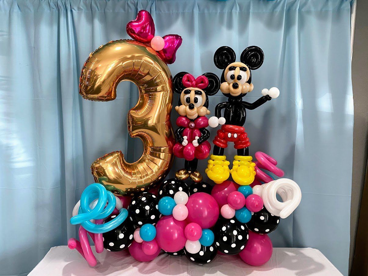 Mickey mouse and minnie mouse made out of balloons are sitting on top of a table.