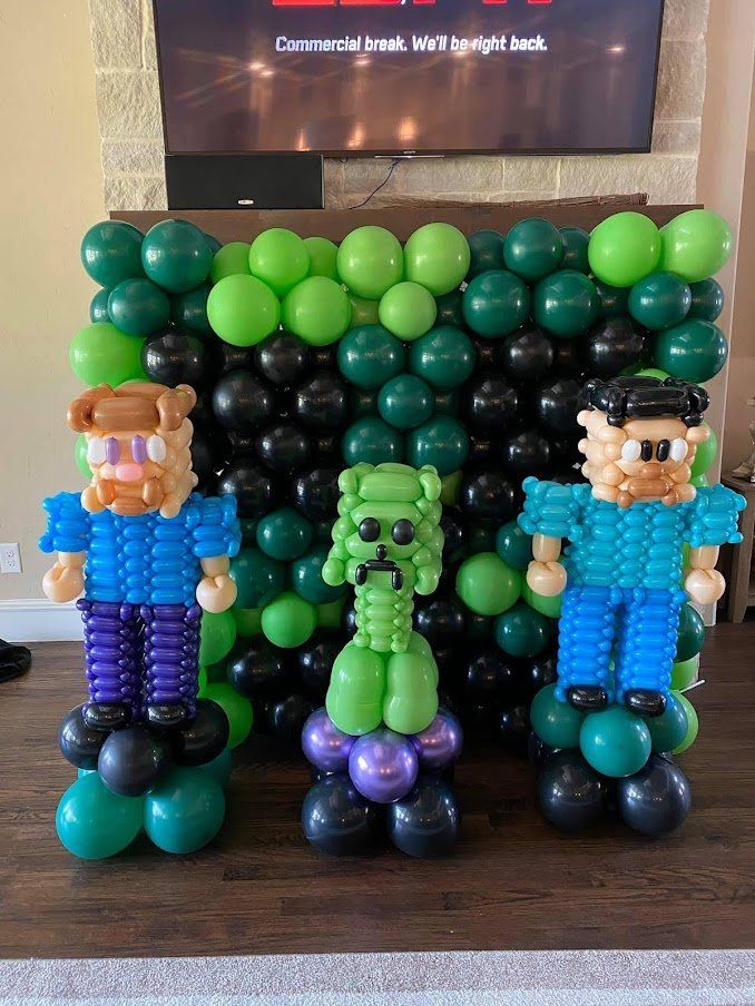 A group of balloons shaped like minecraft characters are sitting in front of a wall.