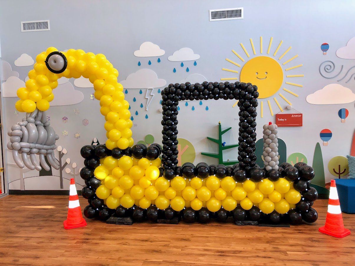 A bulldozer made out of balloons is sitting on a wooden floor.