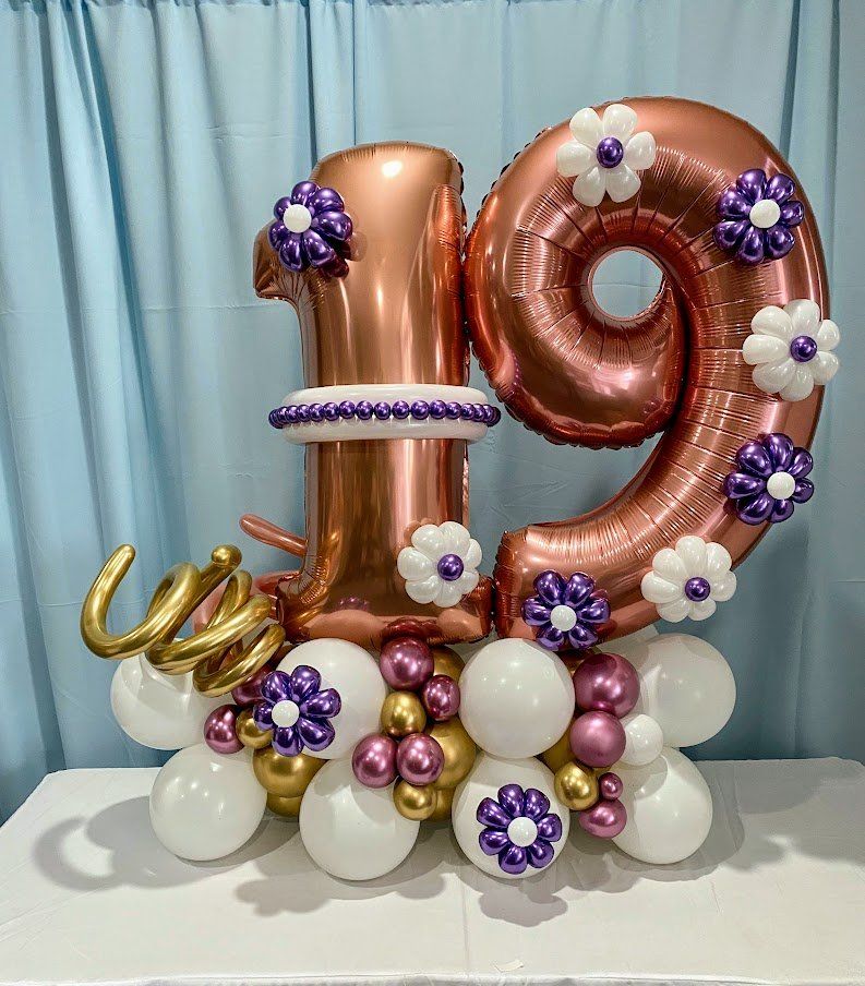 The number 19 is surrounded by balloons and flowers on a table.