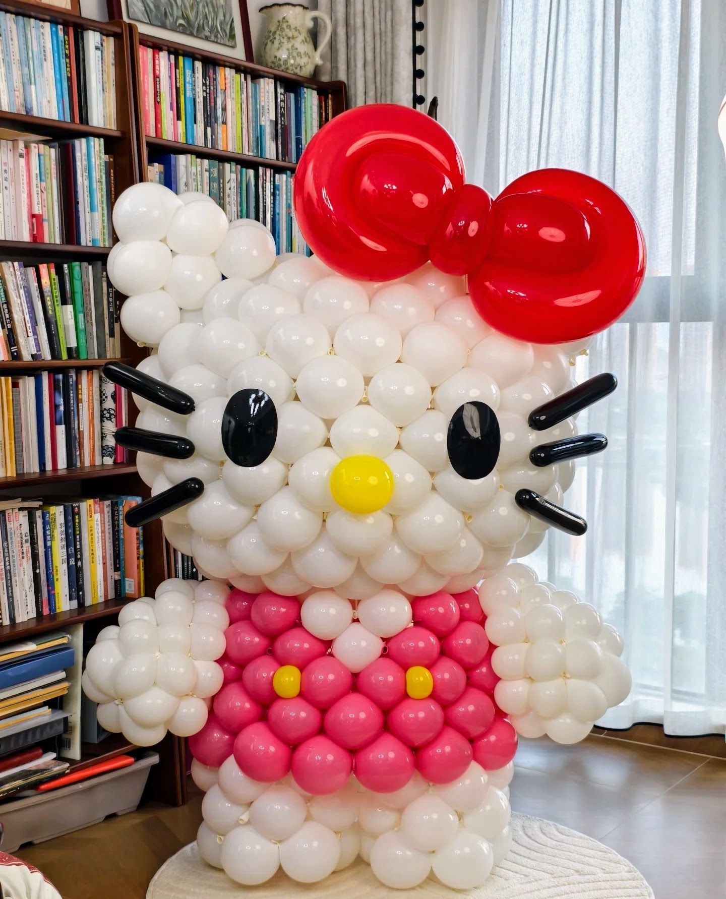 Large Hello Kitty balloon sculpture made of white, pink, red, and black latex balloons with signature red bow, yellow nose, black whiskers and eyes, perfect kawaii birthday party centerpiece or Sanrio themed decoration