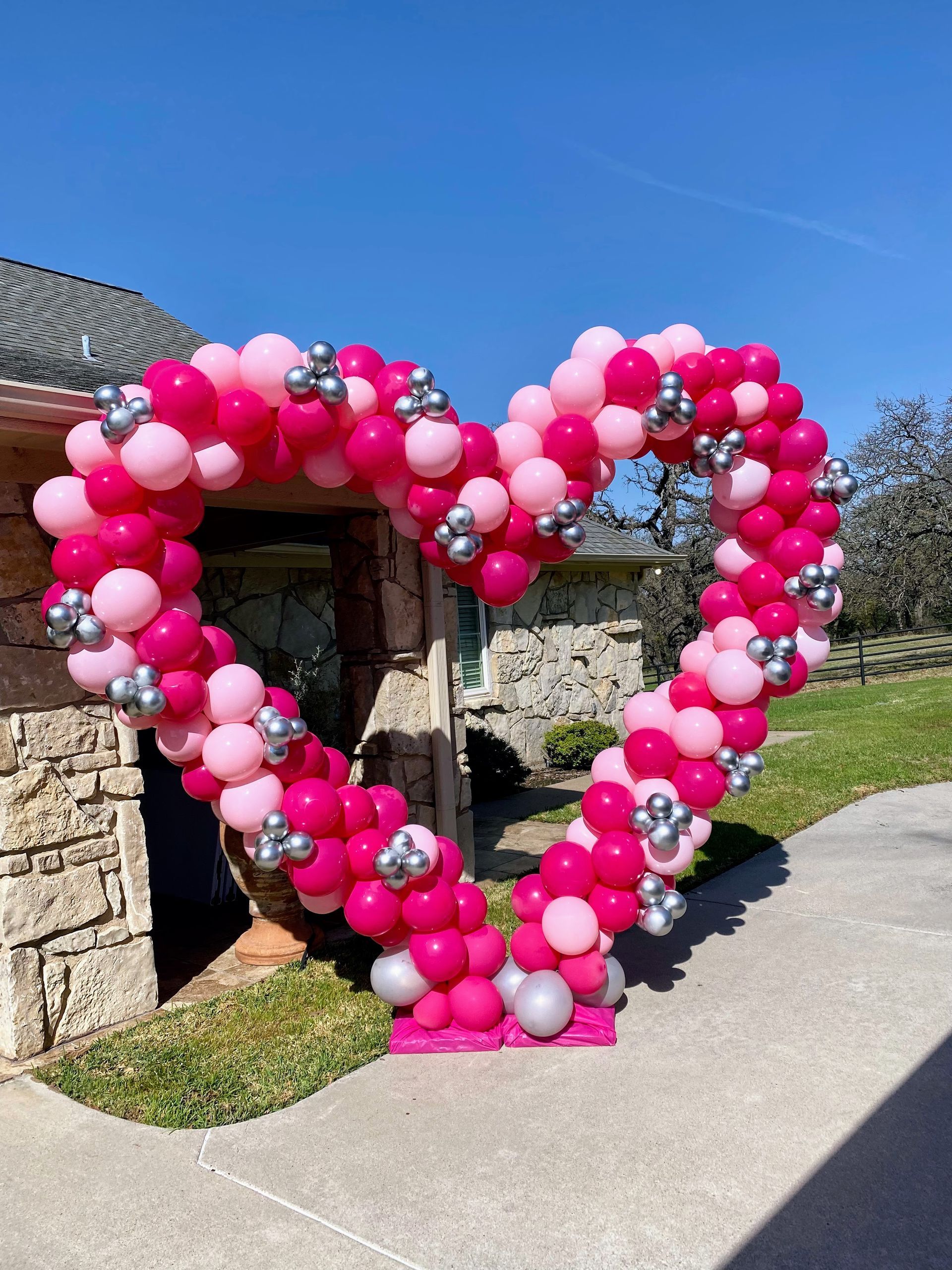 A heart made of pink and silver balloons in front of a house