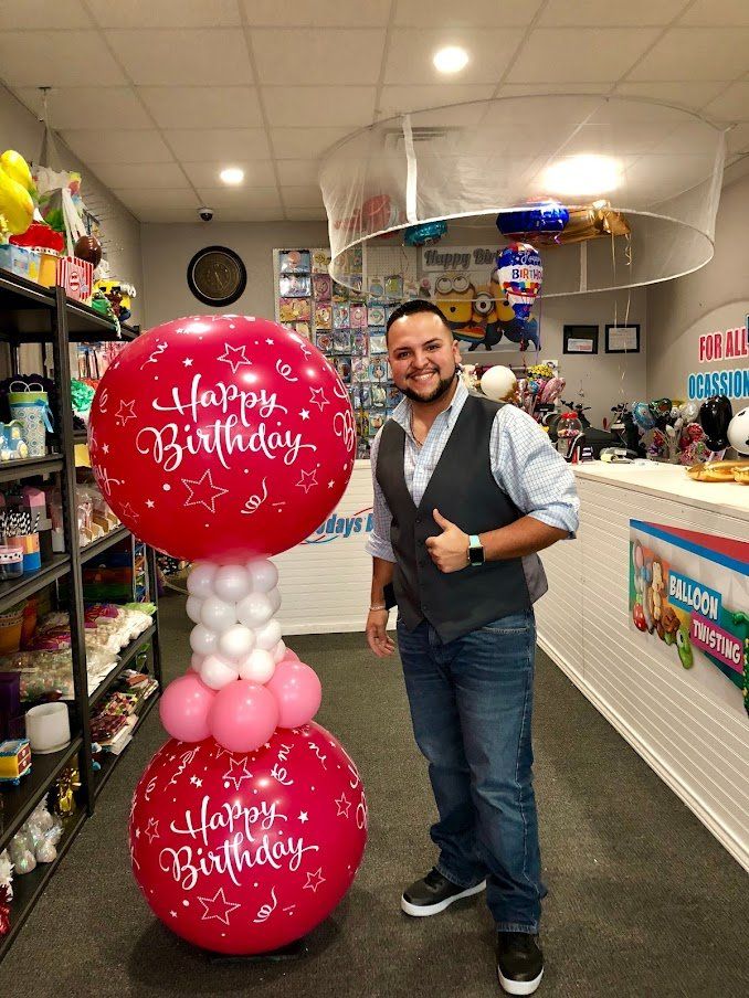 A man is standing next to two balloons that say happy birthday
