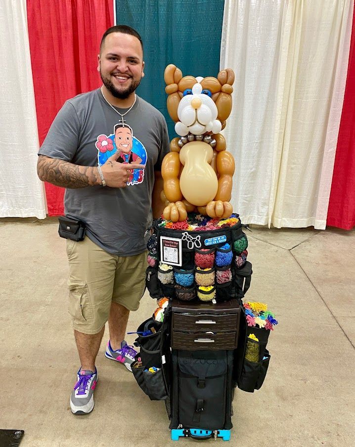 A man is standing next to a balloon dog on top of a suitcase.