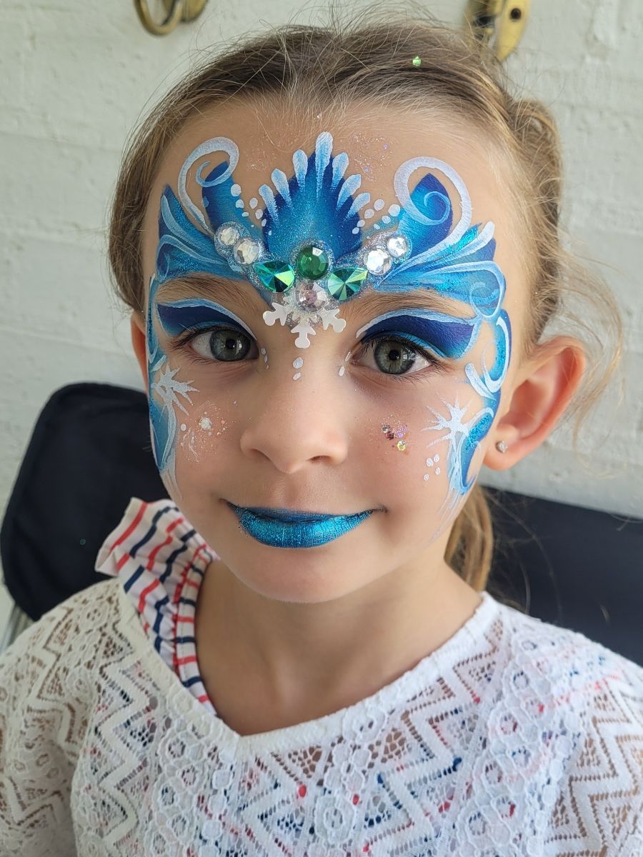 A little girl with her face painted in blue and white.