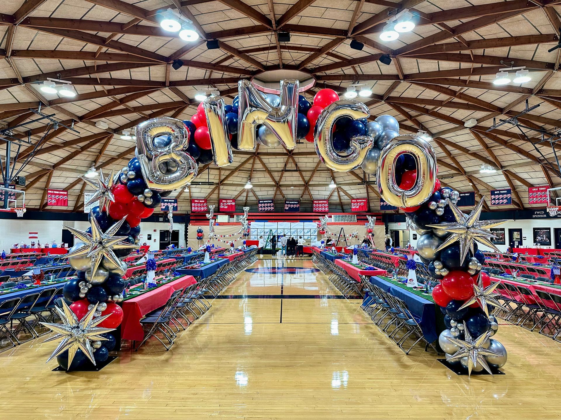 A red , blue and gold balloon arch is in front of a building.