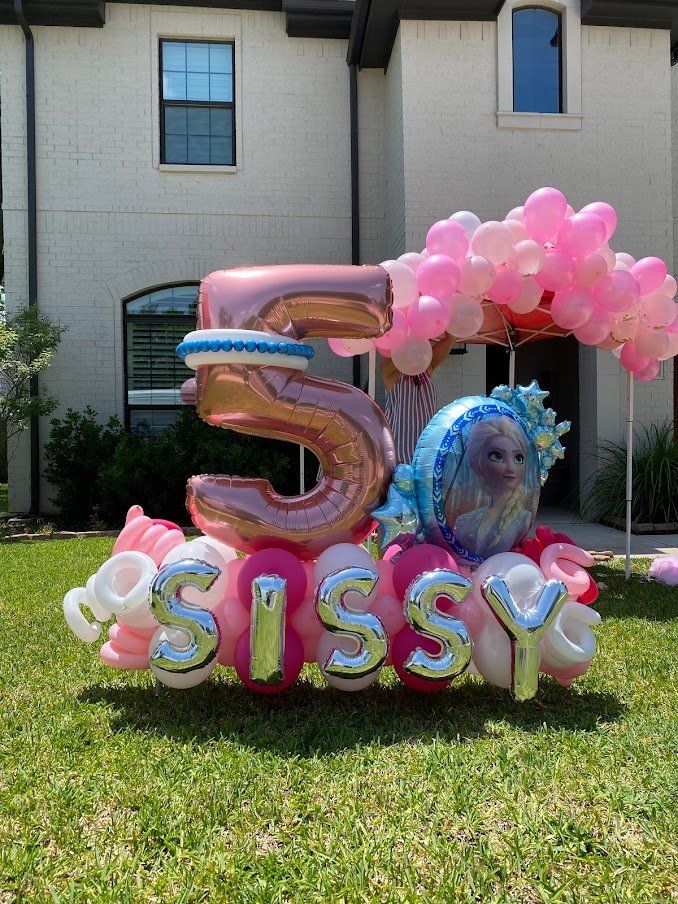 A bunch of balloons are sitting on the grass in front of a house.