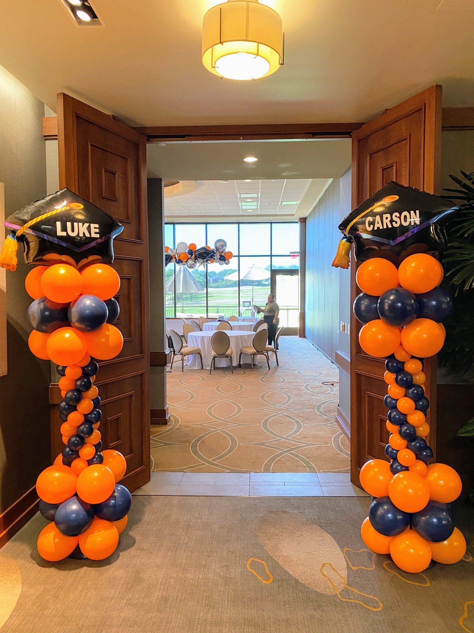 Two columns of orange and blue balloons with graduation caps on them are in a hallway.