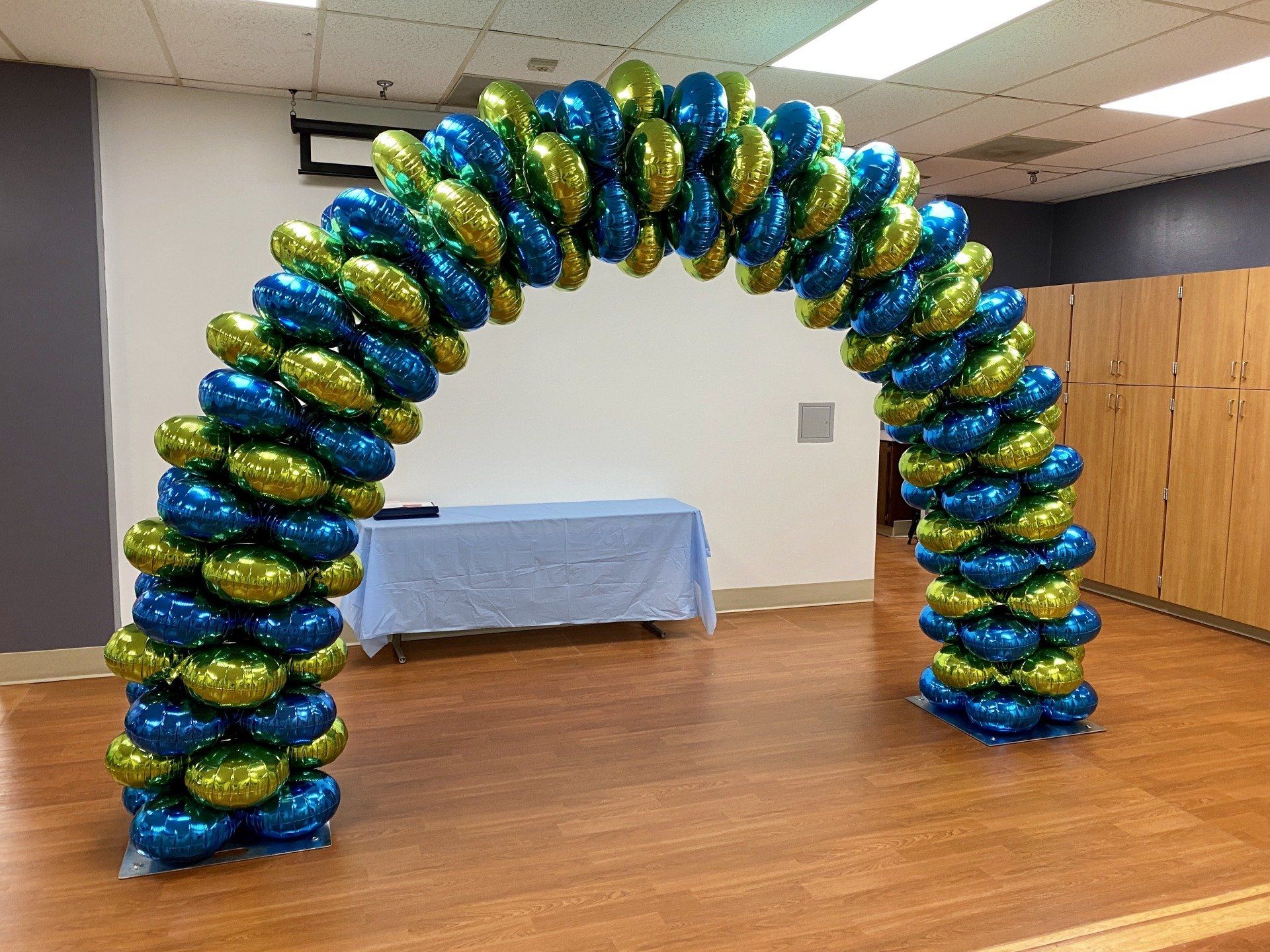 A large arch made of blue and green balloons in a room.