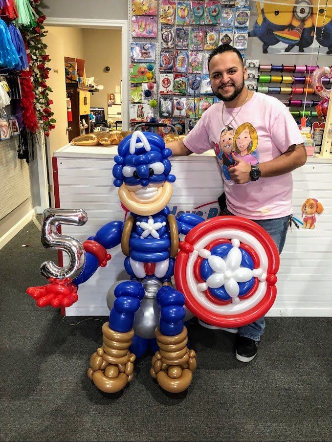 A man is standing next to a captain america made out of balloons.