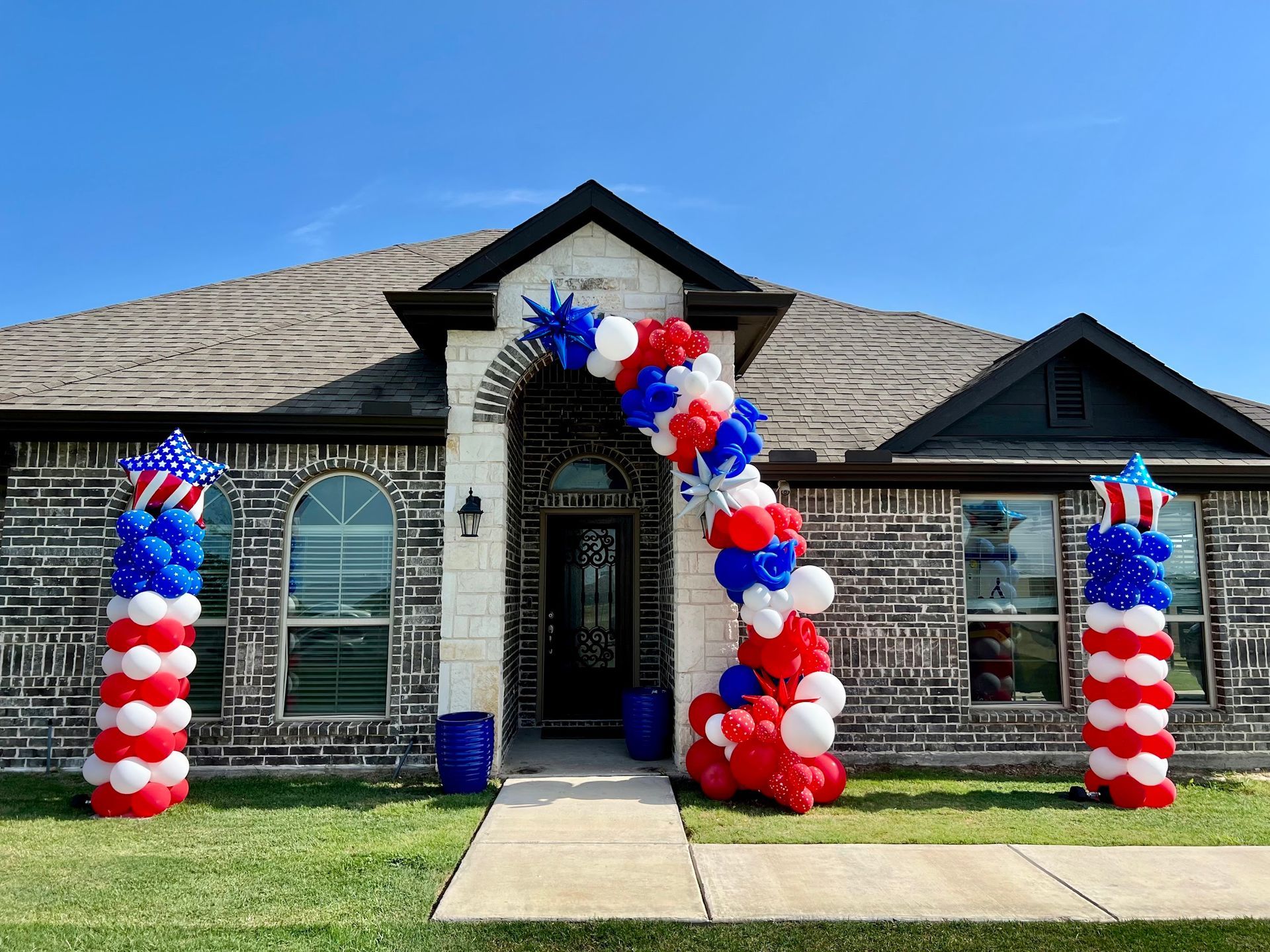 A house is decorated with red , white and blue balloons.