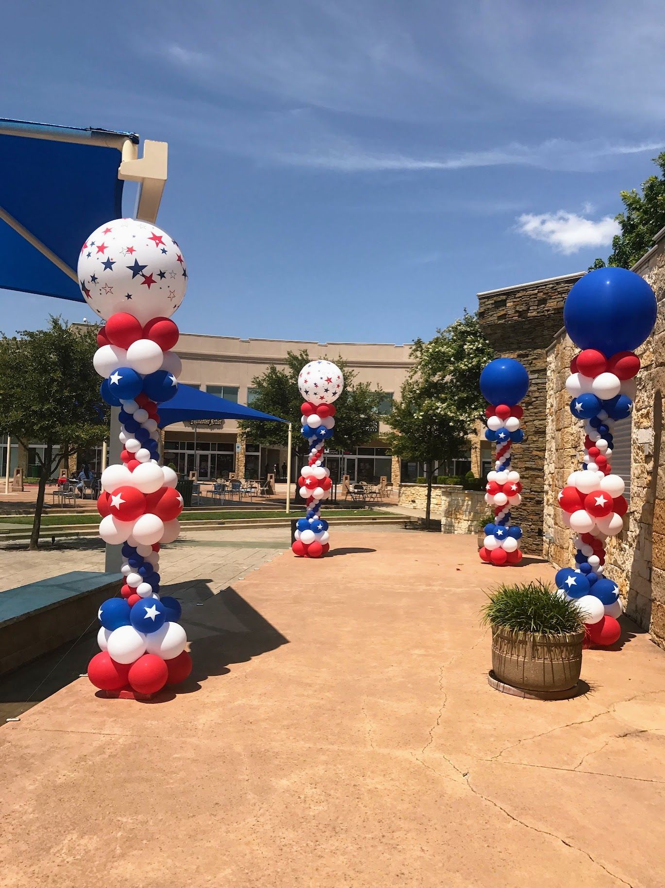 A row of red , white and blue balloons on columns in a park.