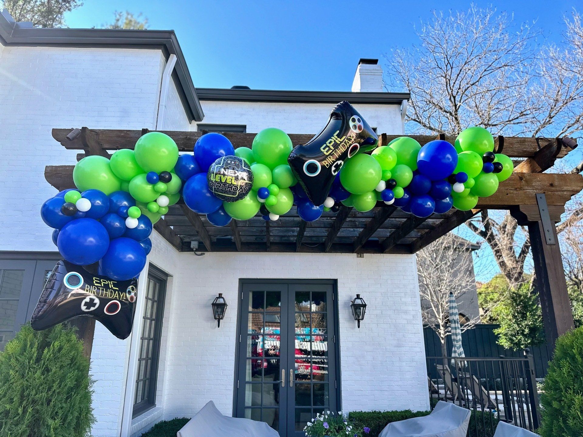 A white house with blue and green balloons hanging from a pergola.