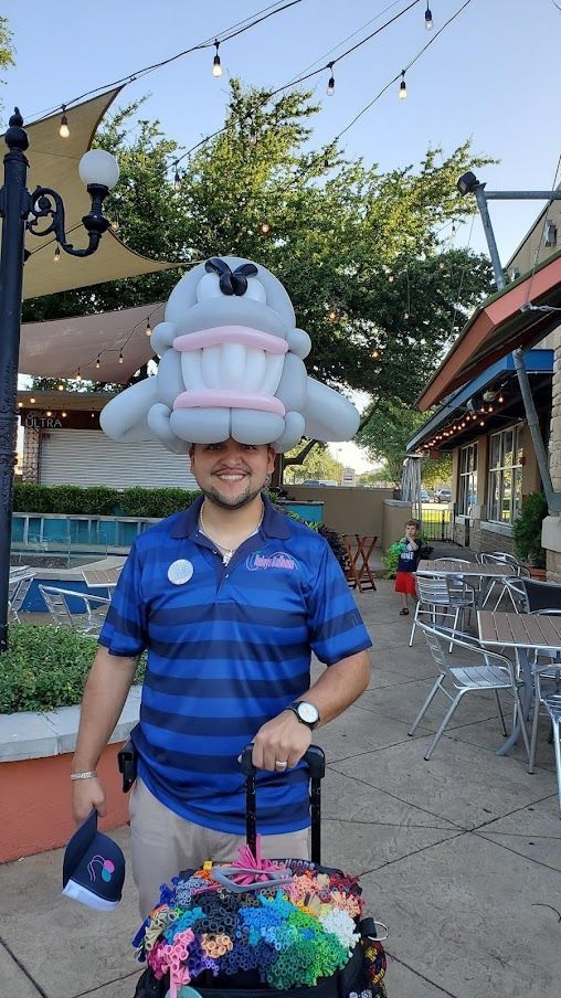 A man wearing a balloon hat is standing next to a suitcase.