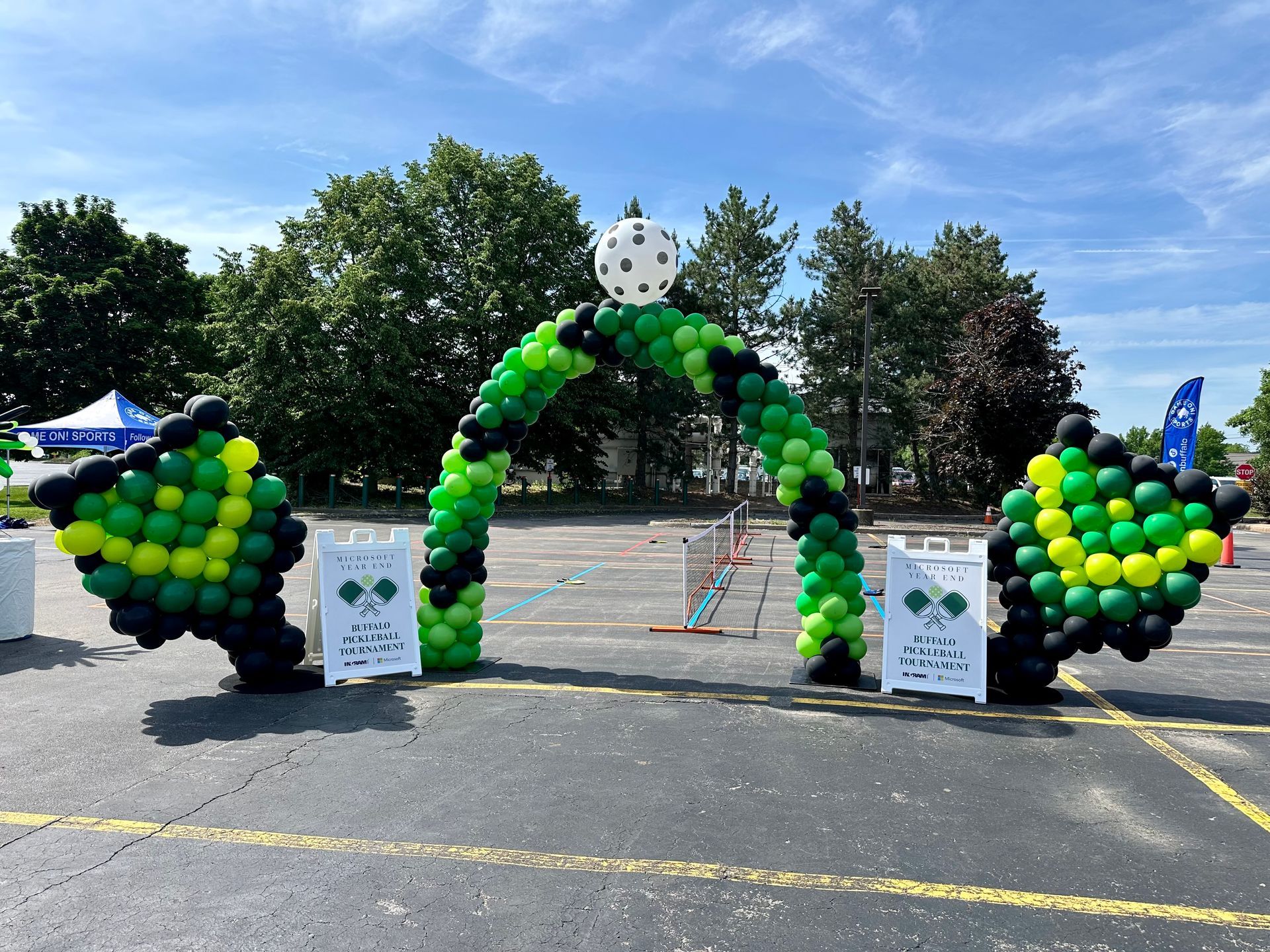 A green and black balloon arch in a parking lot.
