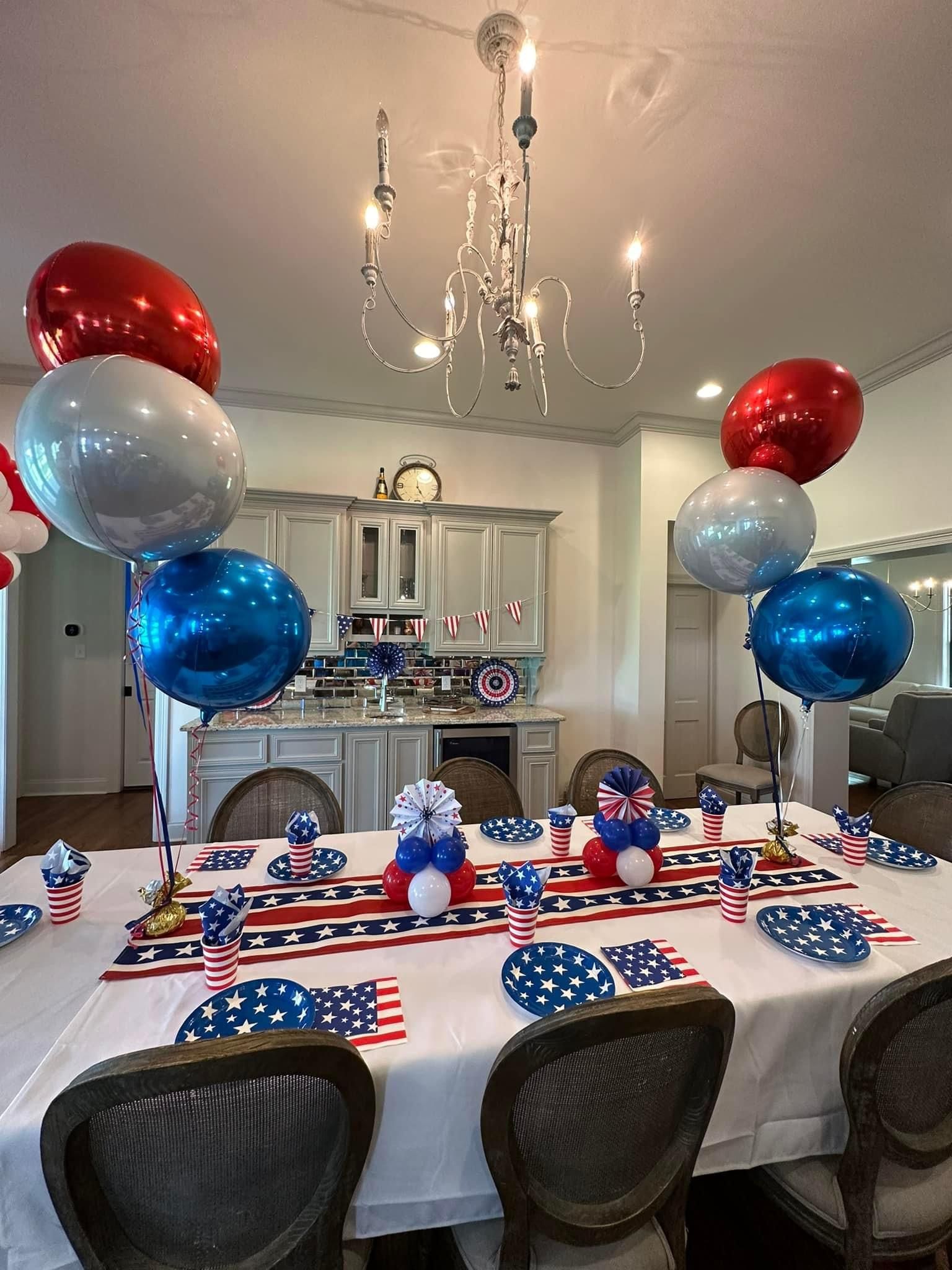 A dining room table decorated for a fourth of july party with red , white and blue balloons.
