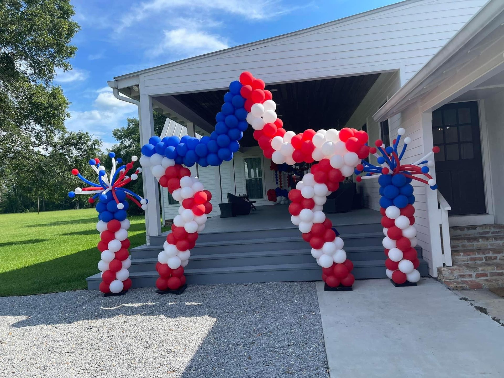 A red , white and blue balloon archway in front of a house.