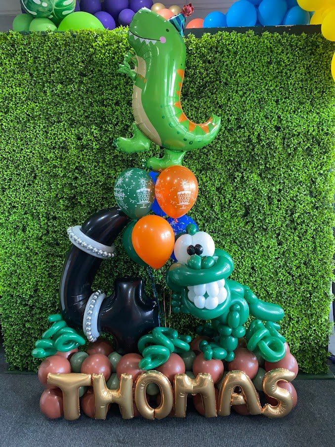 A bunch of balloons are stacked on top of each other in the shape of a dinosaur and the name thomas.