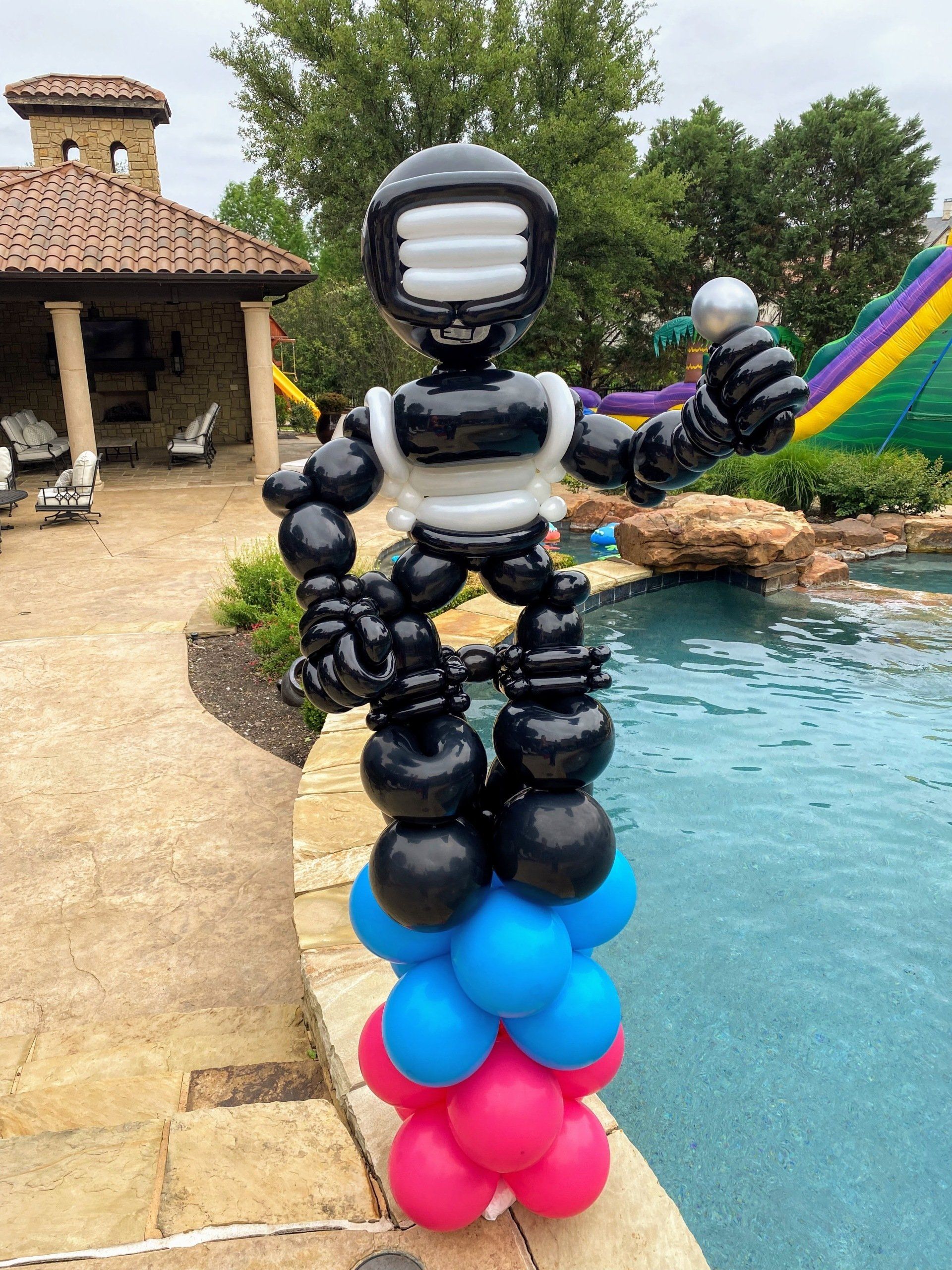 A robot made out of balloons is standing next to a pool.
