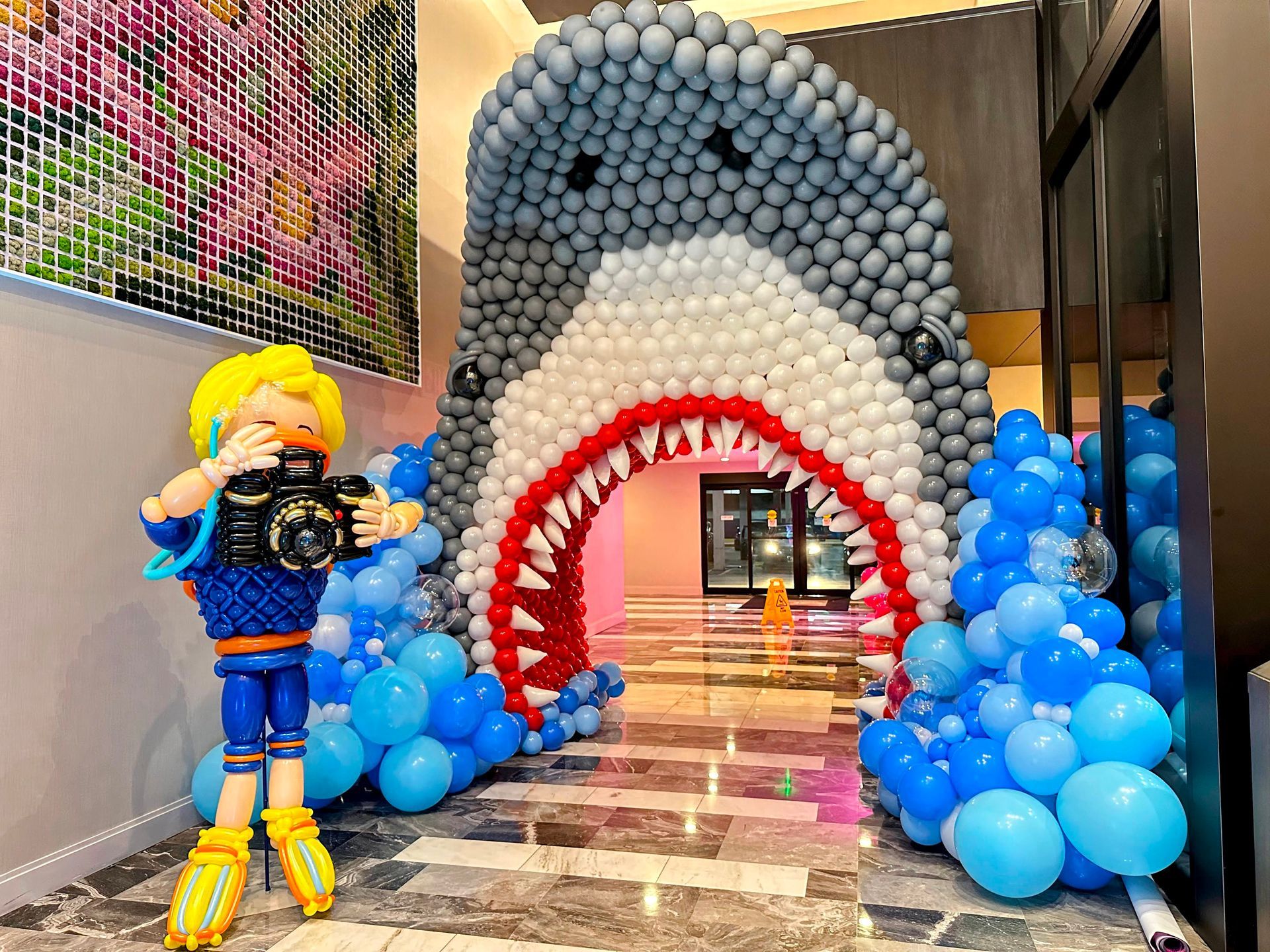 balloon sculpture of a shark in a hotel lobby with a balloon sculpture of a scuba diver holding a balloon camera sculpture