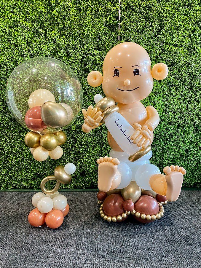 A baby made out of balloons is holding a bottle and a pacifier.