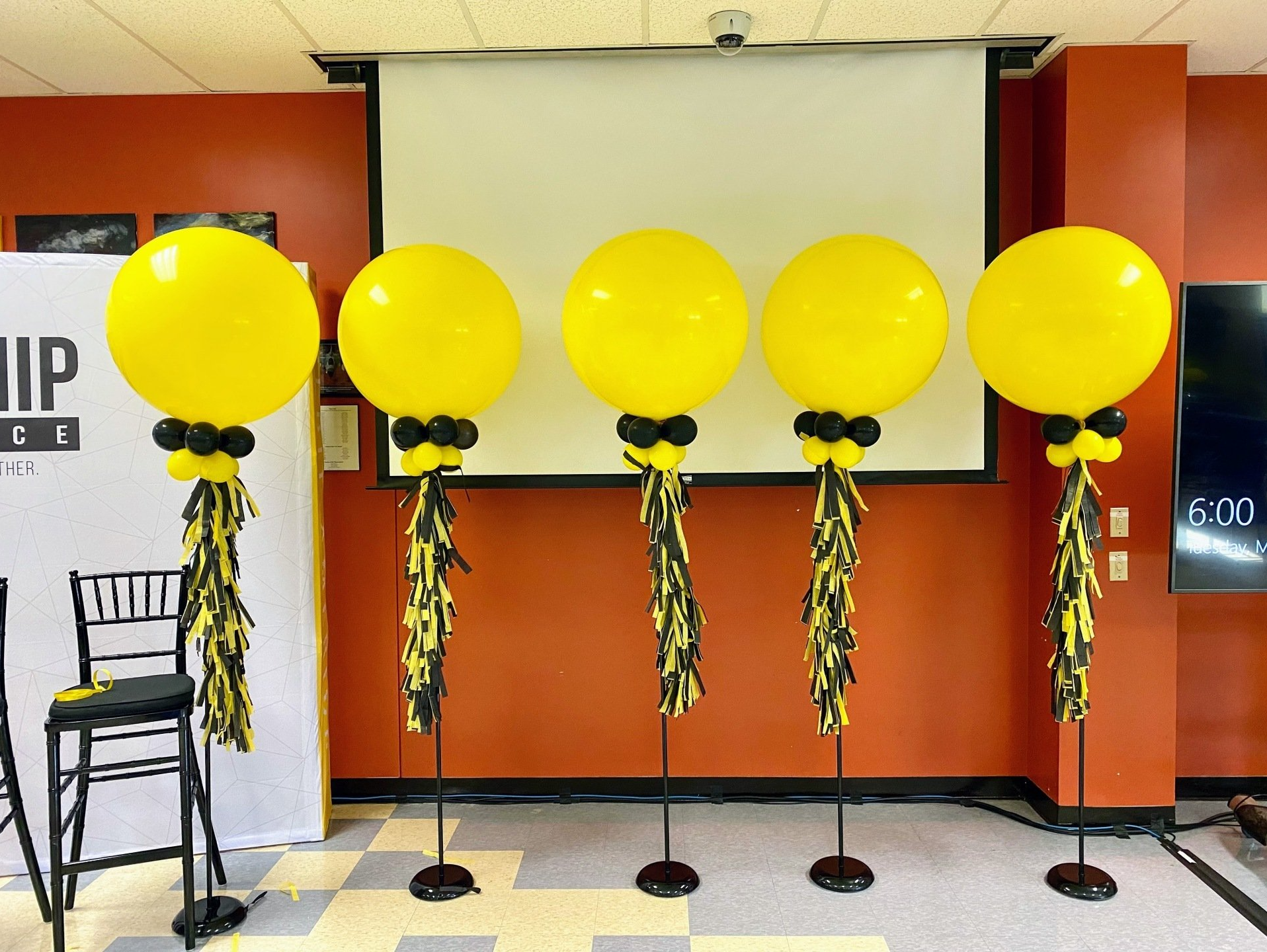 Four yellow balloons are lined up in front of a projector screen