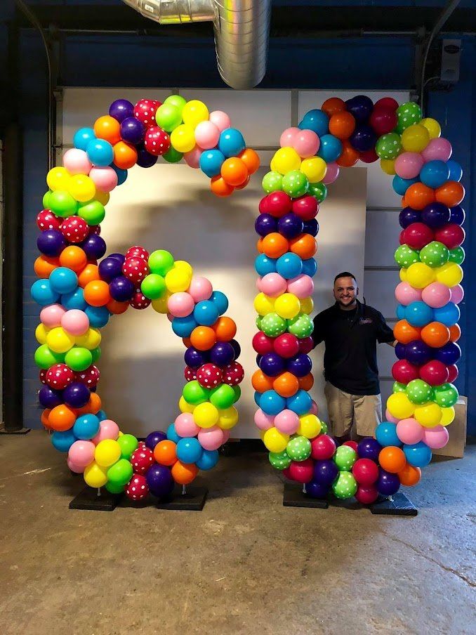 A man stands in front of a large letter g made of balloons