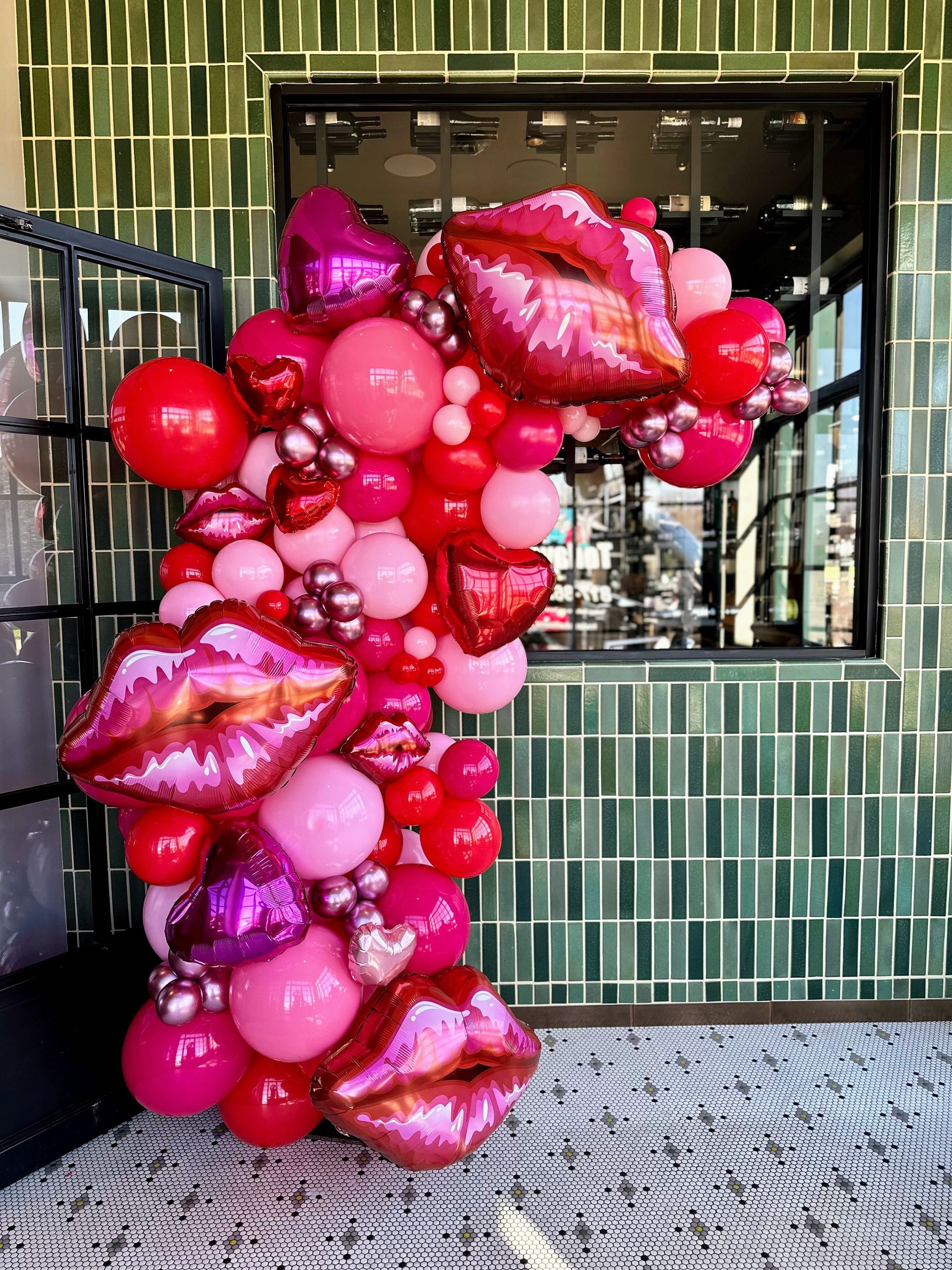 A bunch of balloons shaped like lips and hearts are sitting in front of a window.