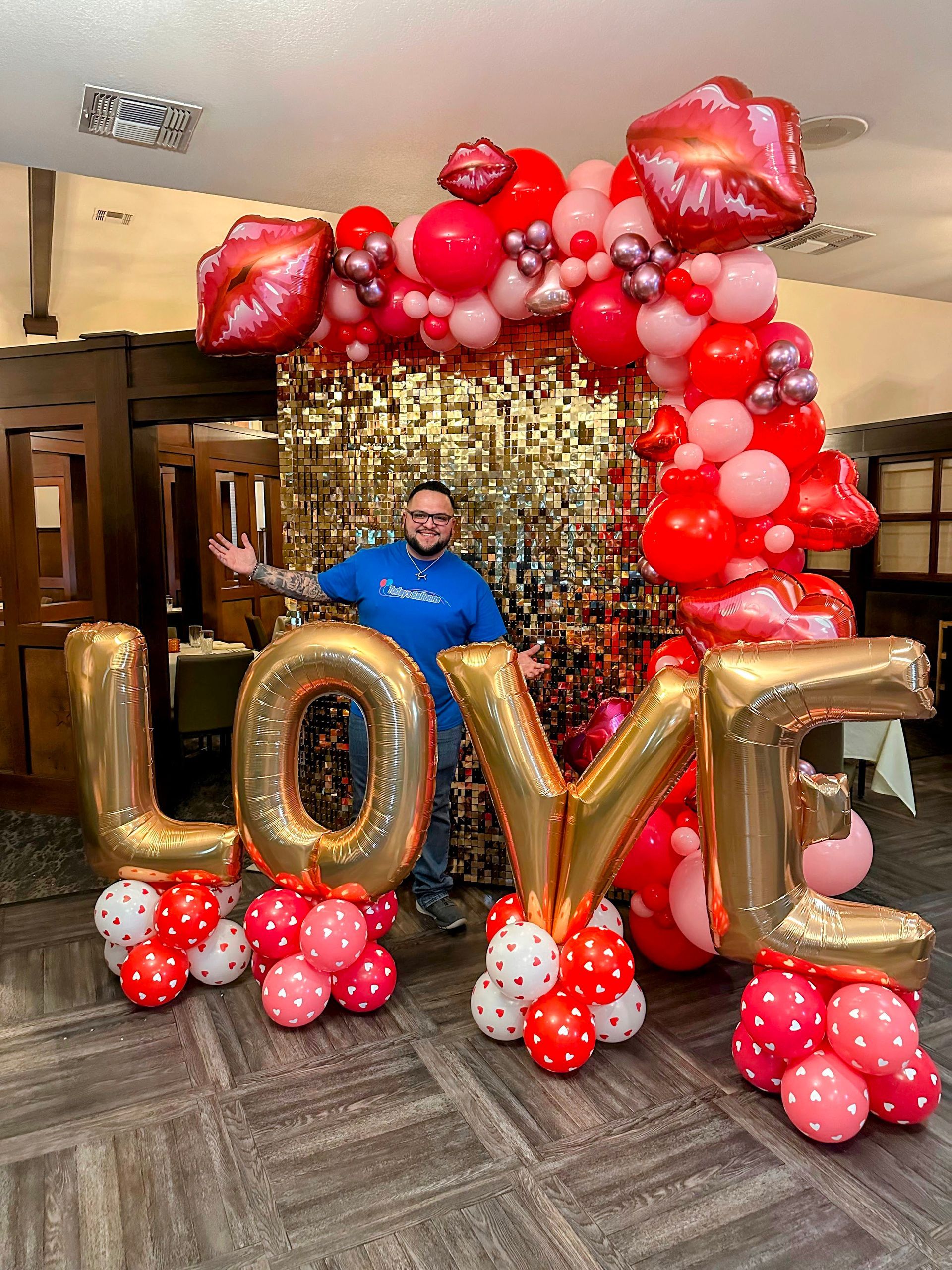 LOVE balloon photo booth frame in red, pink, rose gold, and metallic chrome with giant gold foil 'LOVE' letters, oversized red foil lips, heart accents, organic balloon garland arch, shimmering gold sequin backdrop, perfect for Valentine's Day party, anniversary, proposal, engagement, or romantic event photo op