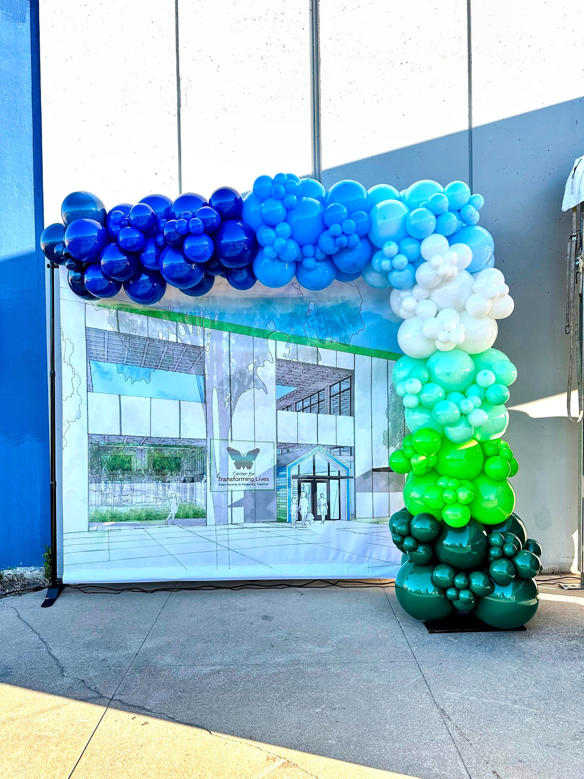 A blue , white , and green balloon arch is sitting in front of a building.