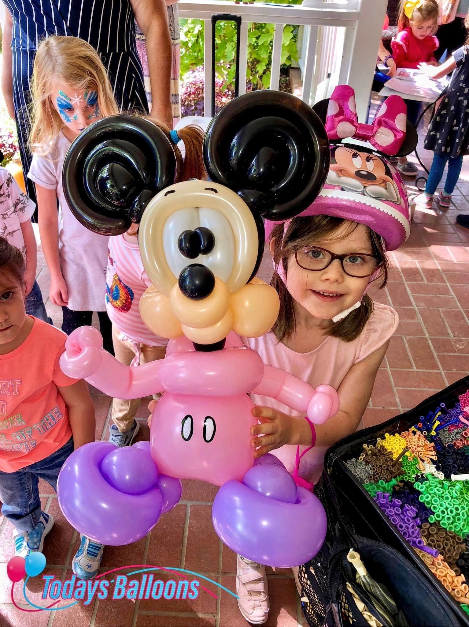 A little girl is holding a mickey mouse made out of balloons.