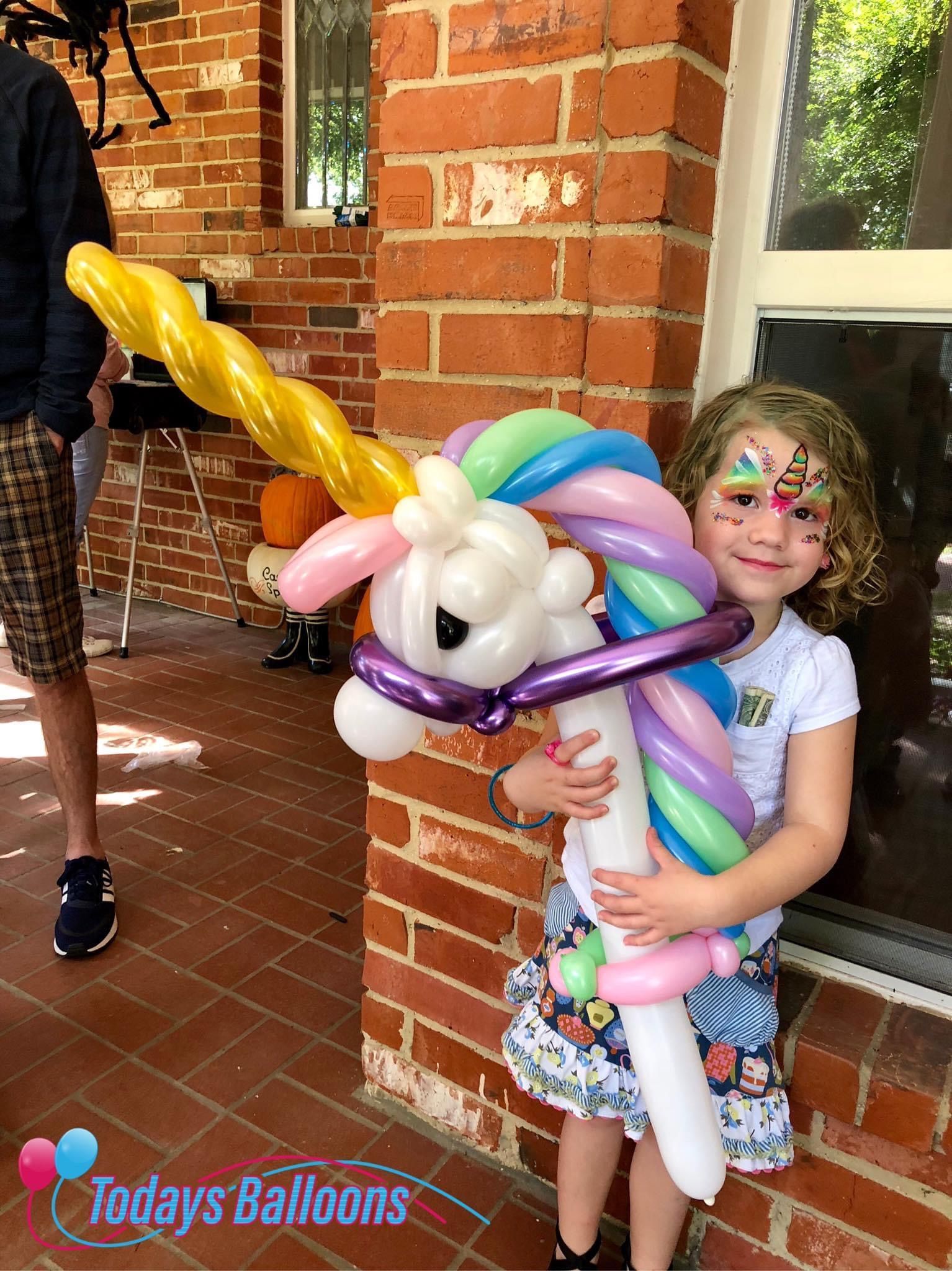 A little girl is holding a balloon shaped like a unicorn.