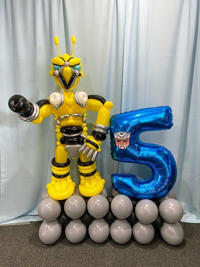 A robot made out of balloons is standing next to a number 5 balloon.