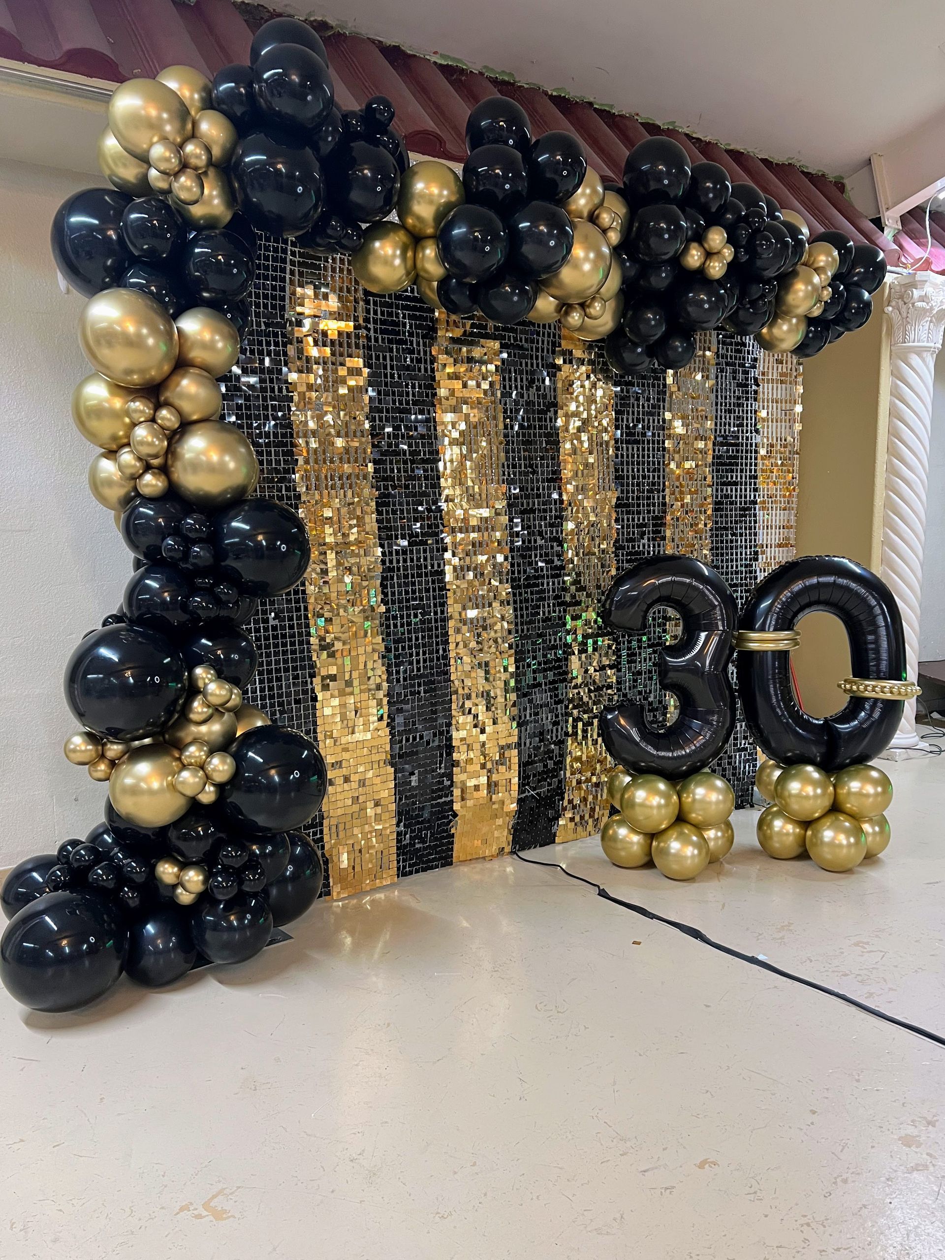 A wall decorated with black and gold balloons and the number 30.